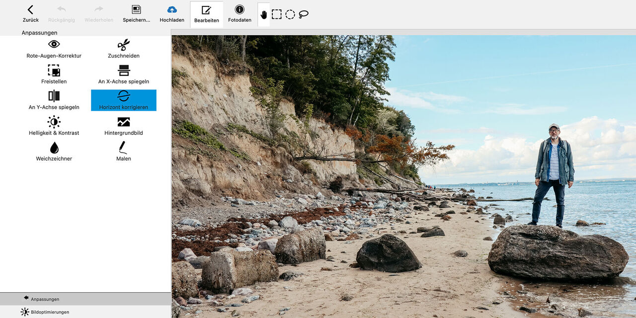 Ein Mann steht an einem Strand neben großen Steinen, umgeben von Wasser und Bäumen.
