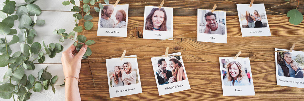 Person hängt Fotos an einer Holztafel, umgeben von Eukalyptus. Freude und Erinnerungen sind sichtbar.