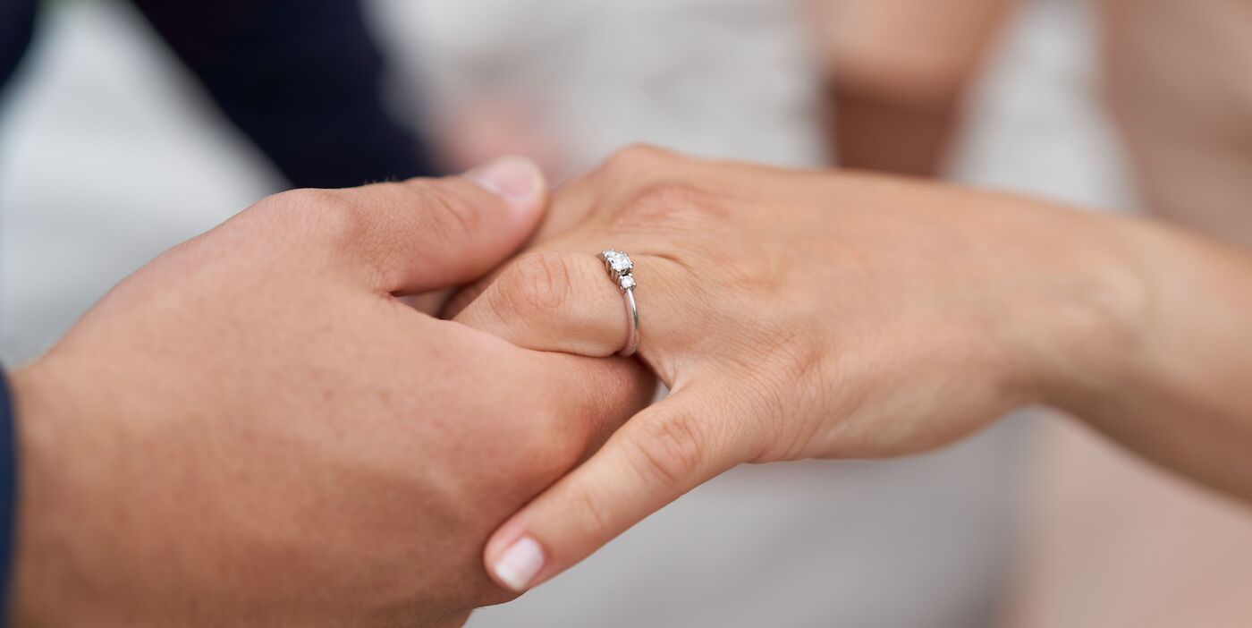 Zwei Hände halten sich. An einer Hand glänzt ein silberner Ring mit drei Steinen