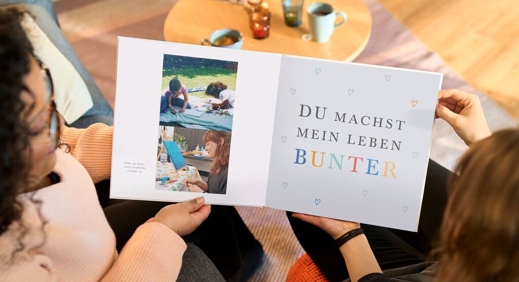 Zwei Personen betrachten gemeinsam ein Fotobuch mit bunten Seiten.