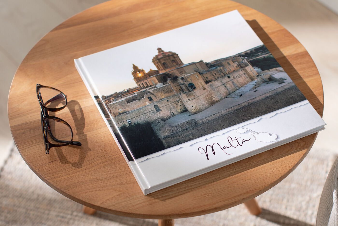 Ein Fotobuch mit dem Titel 'Malta' liegt auf einem Tisch neben einer Brille.