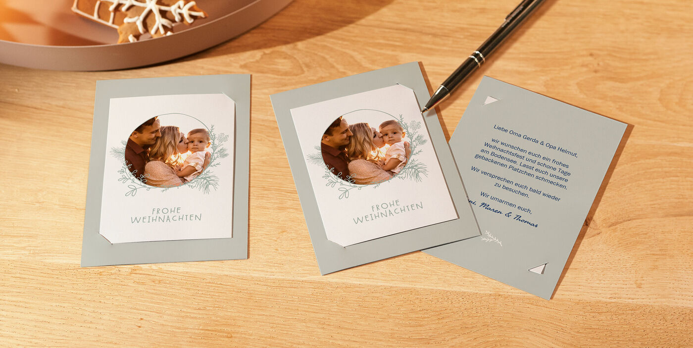 Drei CEWE Karten mit Einsteckfotos auf Holztisch, zwei mit Rundfoto Frohe Weihnachten und eine mit Innentext