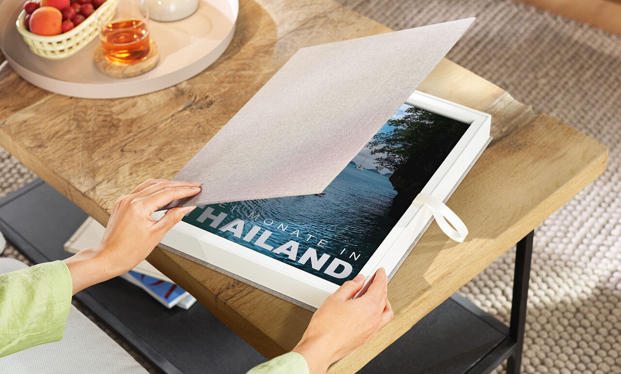 Person öffnet Geschenkbox mit CEWE FOTOBUCH Thailand
