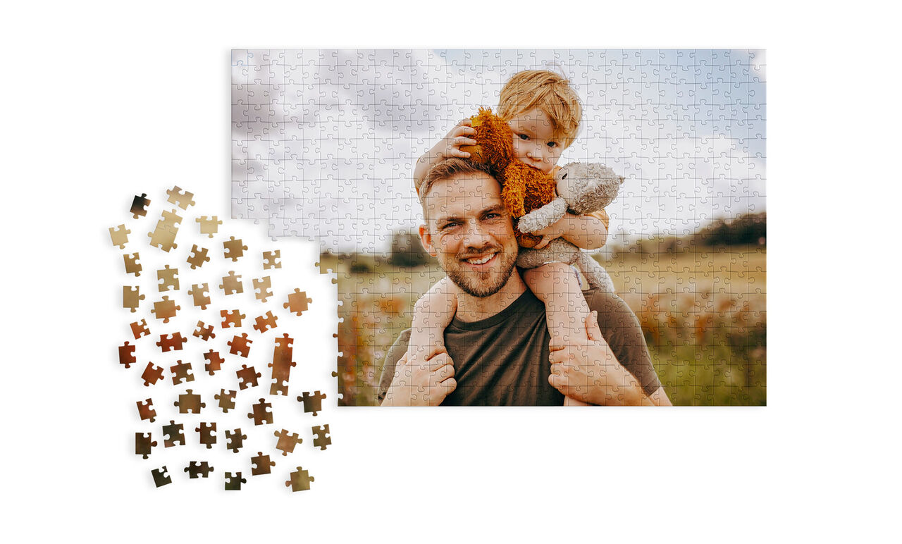 Ein Puzzle zeigt einen Vater mit seinem Kind auf dem Arm, umgeben von einer malerischen Landschaft.