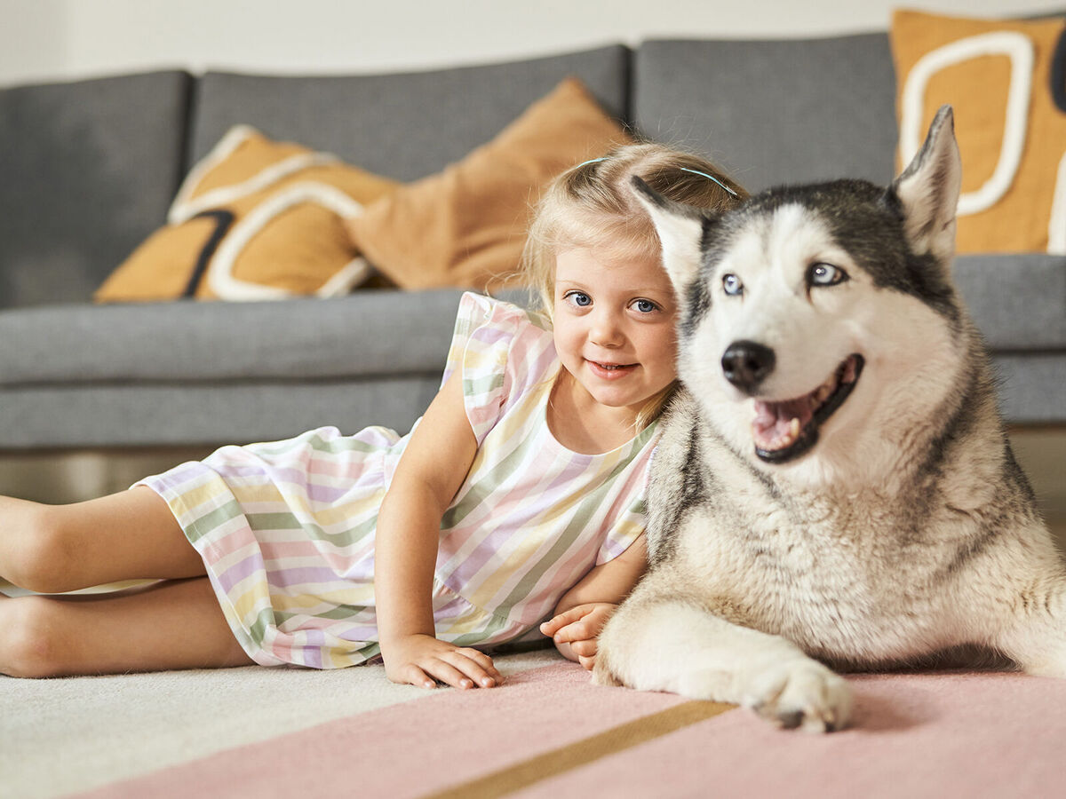 Ein Mädchen und ein Hund liegen zusammen auf einem Teppich.