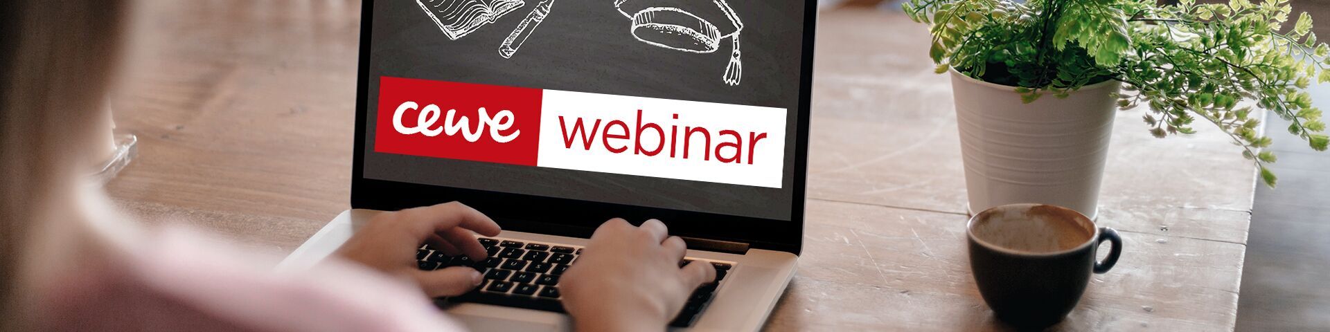 Die Hände einer Person tippen auf der Tastatur eines Laptops, während ein CEWE Webinar auf dem Bildschirm angezeigt wird.