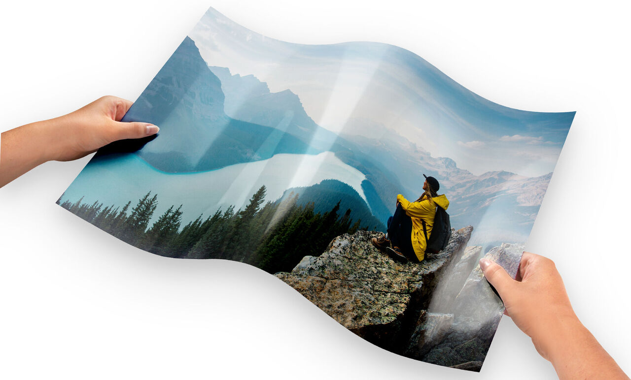 Person in gelber Jacke sitzt auf Felsen und schaut auf einen See und Berge