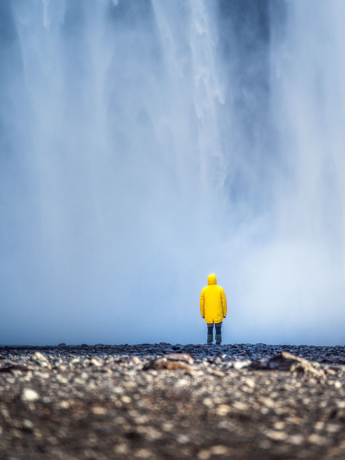 Eine Person in einem gelben Regenmantel steht vor einem Wasserfall und genießt die erfrischende Spritzwasser-Dampfwolke.