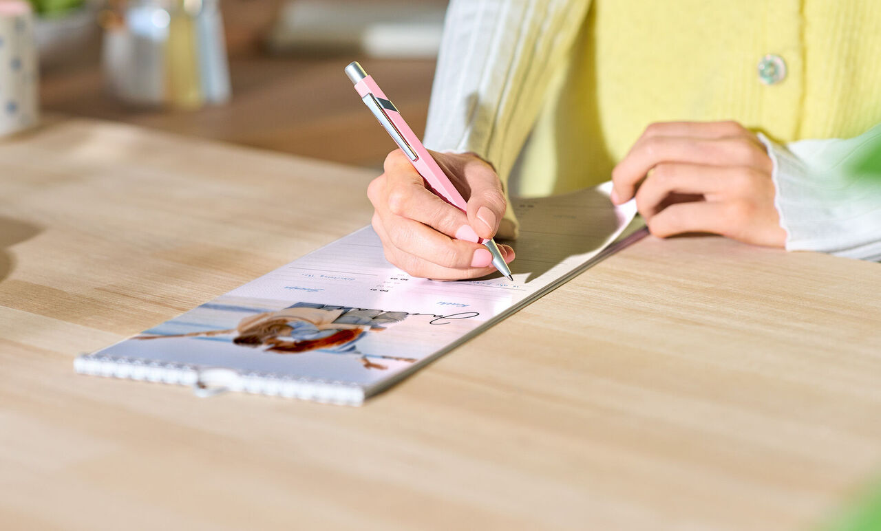 Hand schreibt mit Stift in CEWE Fotokalender mit Strandbild