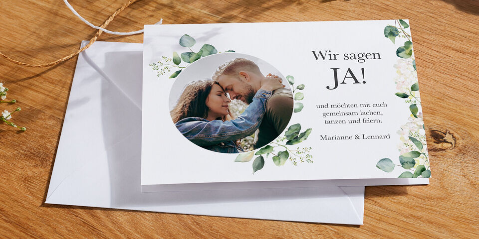 Ein Paar küssend, umgeben von grünen Blättern. Eine Einladung zur Feier.