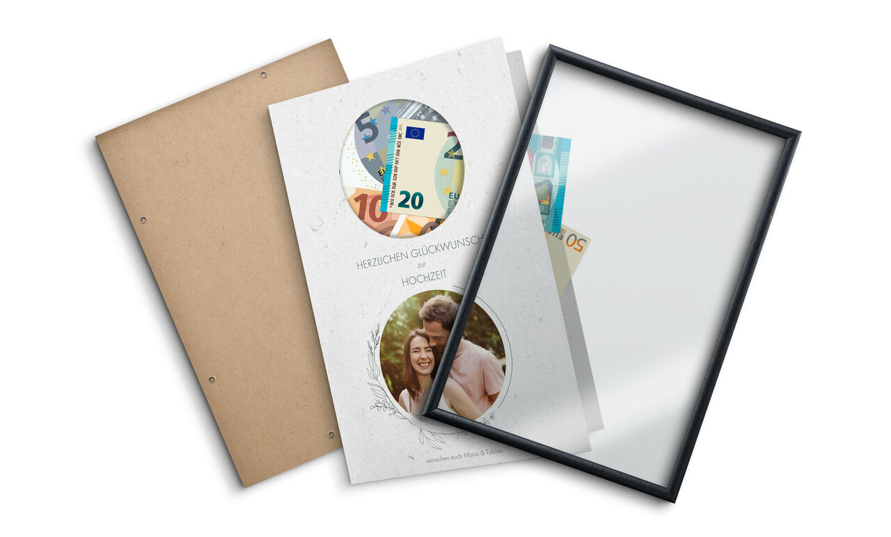Zwei geöffnete CEWE Fotobücher mit Geldscheinen und einem Rahmen.