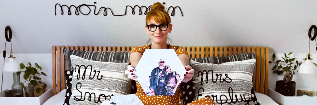 Eine Person auf einem Bett hält ein Wandbild mit einem Foto.