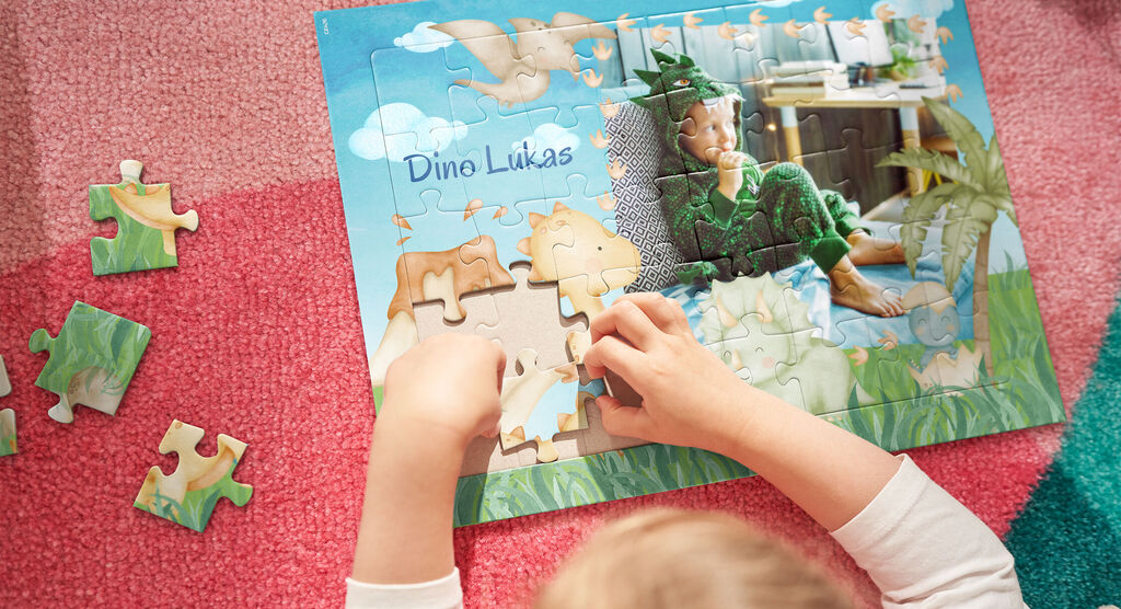 Ein Kind setzt Puzzlestücke in ein personalisiertes Puzzle mit der Aufschrift 'Dino Lukas'.