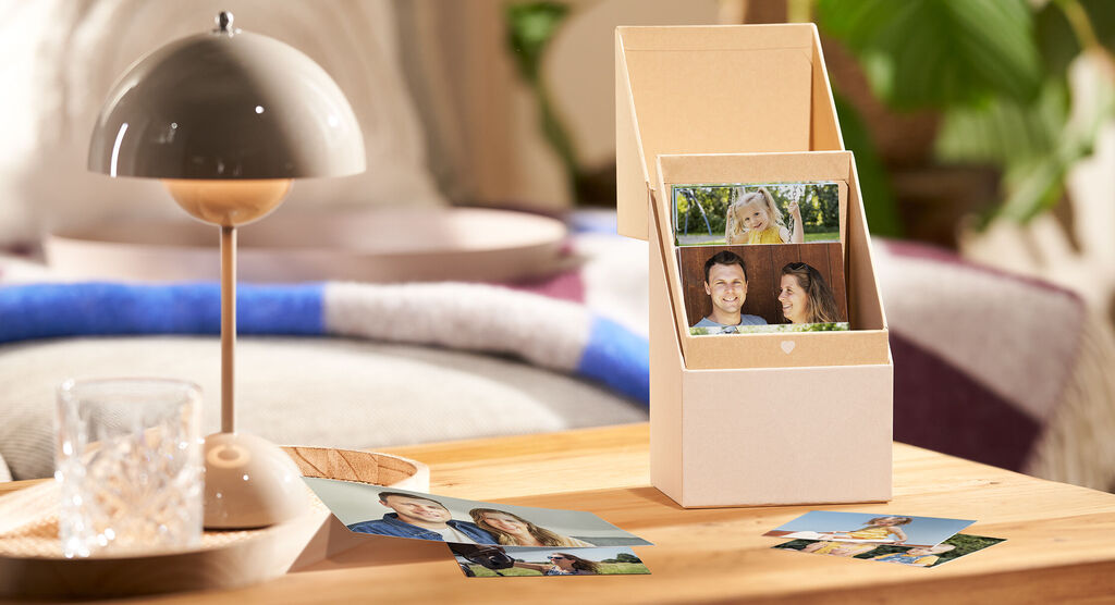 CEWE Fotokarten in einer hübschen Box, umgeben von Fotos auf dem Tisch