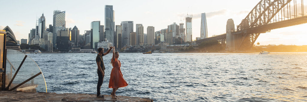 Paar tanzt am Wasser bei Sonnenuntergang mit der Stadt im Hintergrund