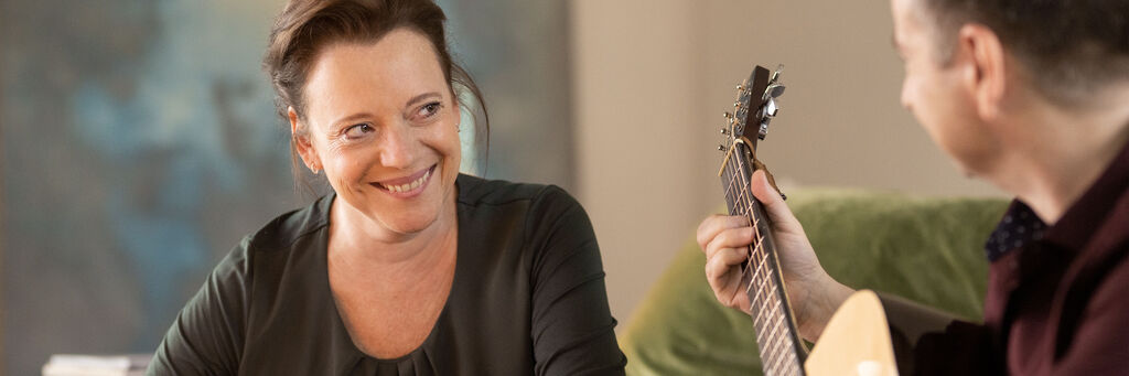 Eine Frau lauscht begeistert einem Mann, der Gitarre spielt. Gemütliche Atmosphäre.