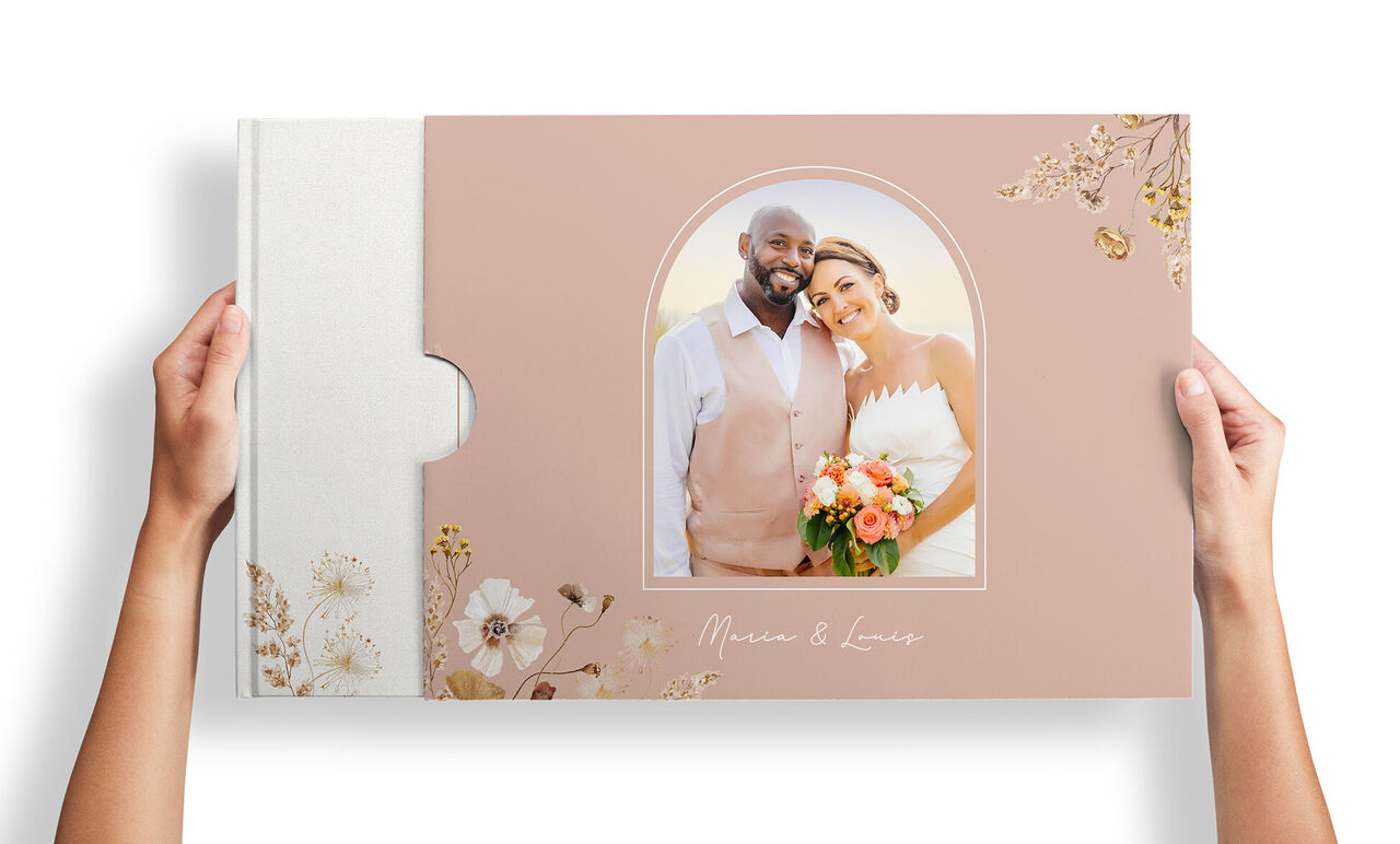 Person hält CEWE FOTOBUCH Hochzeit mit Brautpaarfoto in blumiger Schuberhülle