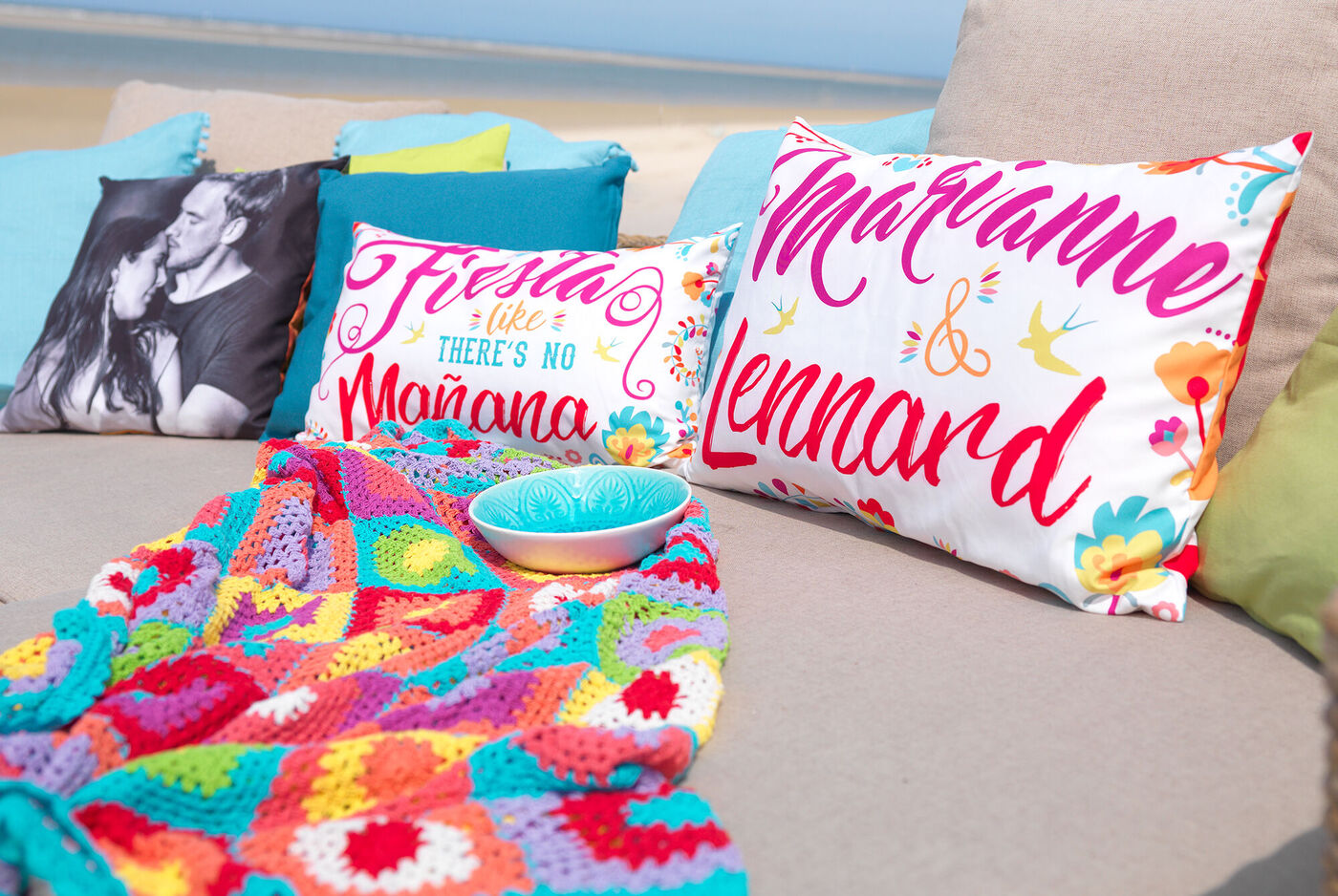 Bunte Kissen mit Namen in fröhlichem Design auf einer Couch am Strand