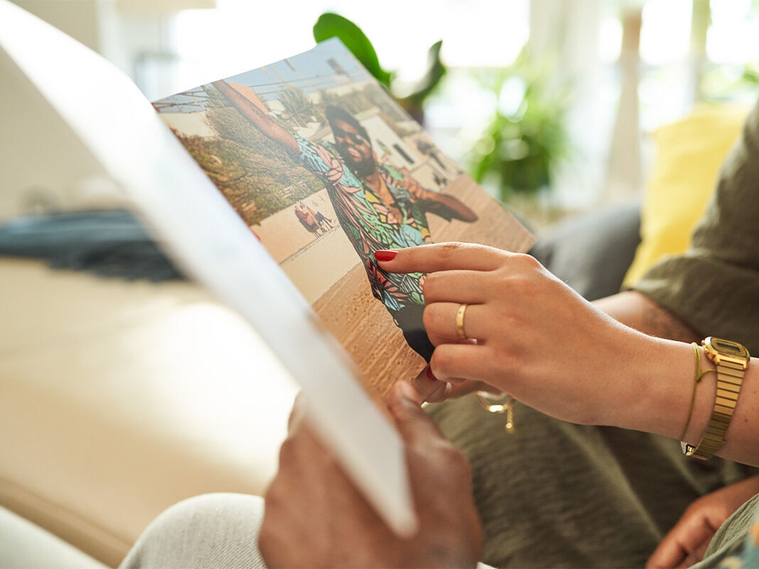 Eine Person zeigt ein Fotobuch und lächelt, während eine andere Person die Seite betrachtet.
