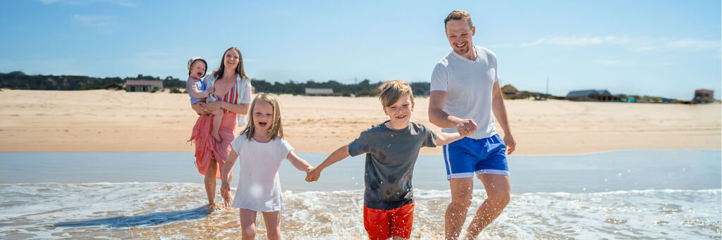Familie spielt glücklich am Strand, mit Wasser, Sonne und Freude