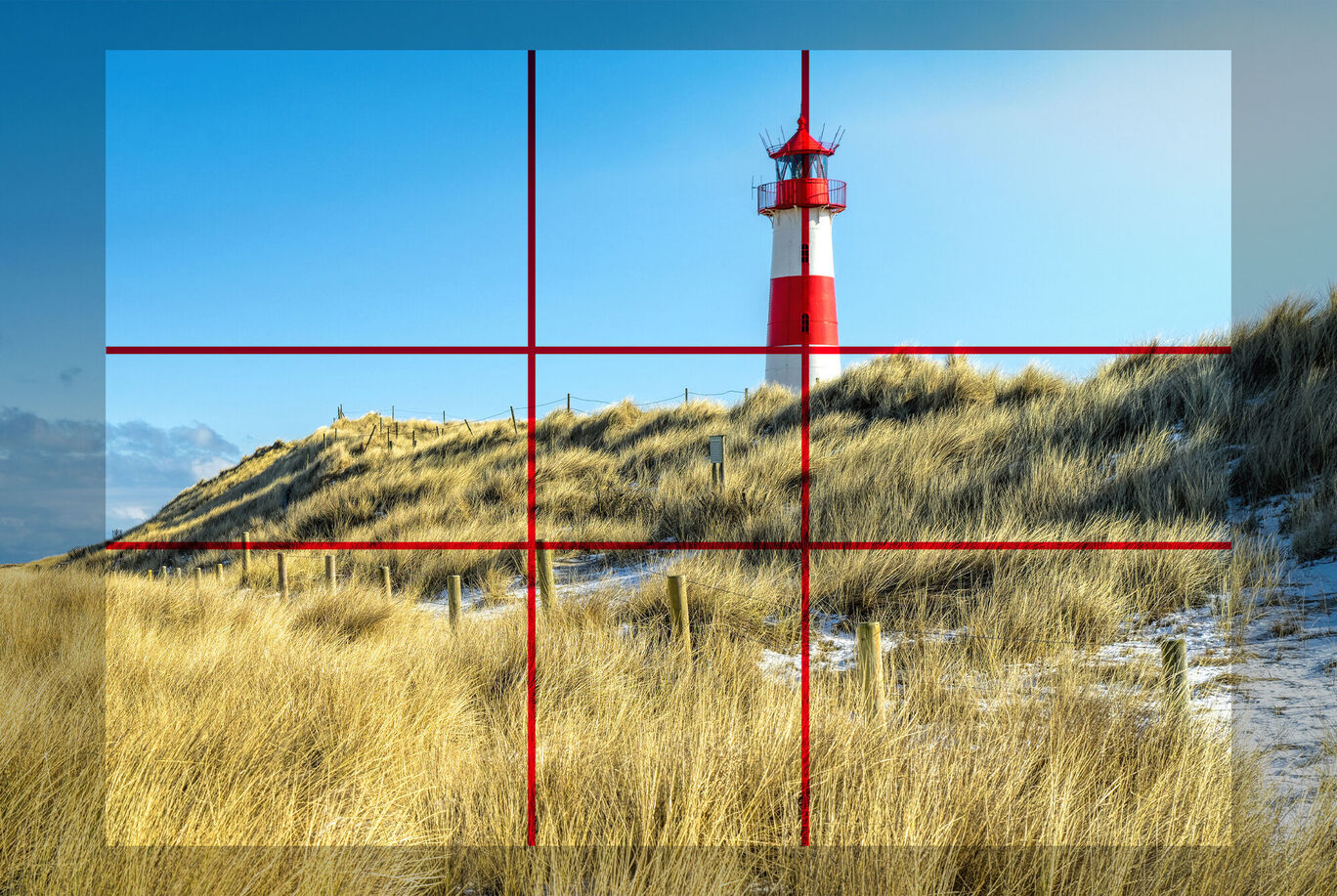 Leuchtturm auf einer Sanddüne, umgeben von hohem Gras und blassem Himmel