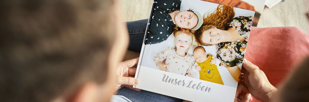 Familie betrachtet ein CEWE Fotobuch mit Erinnerungen.