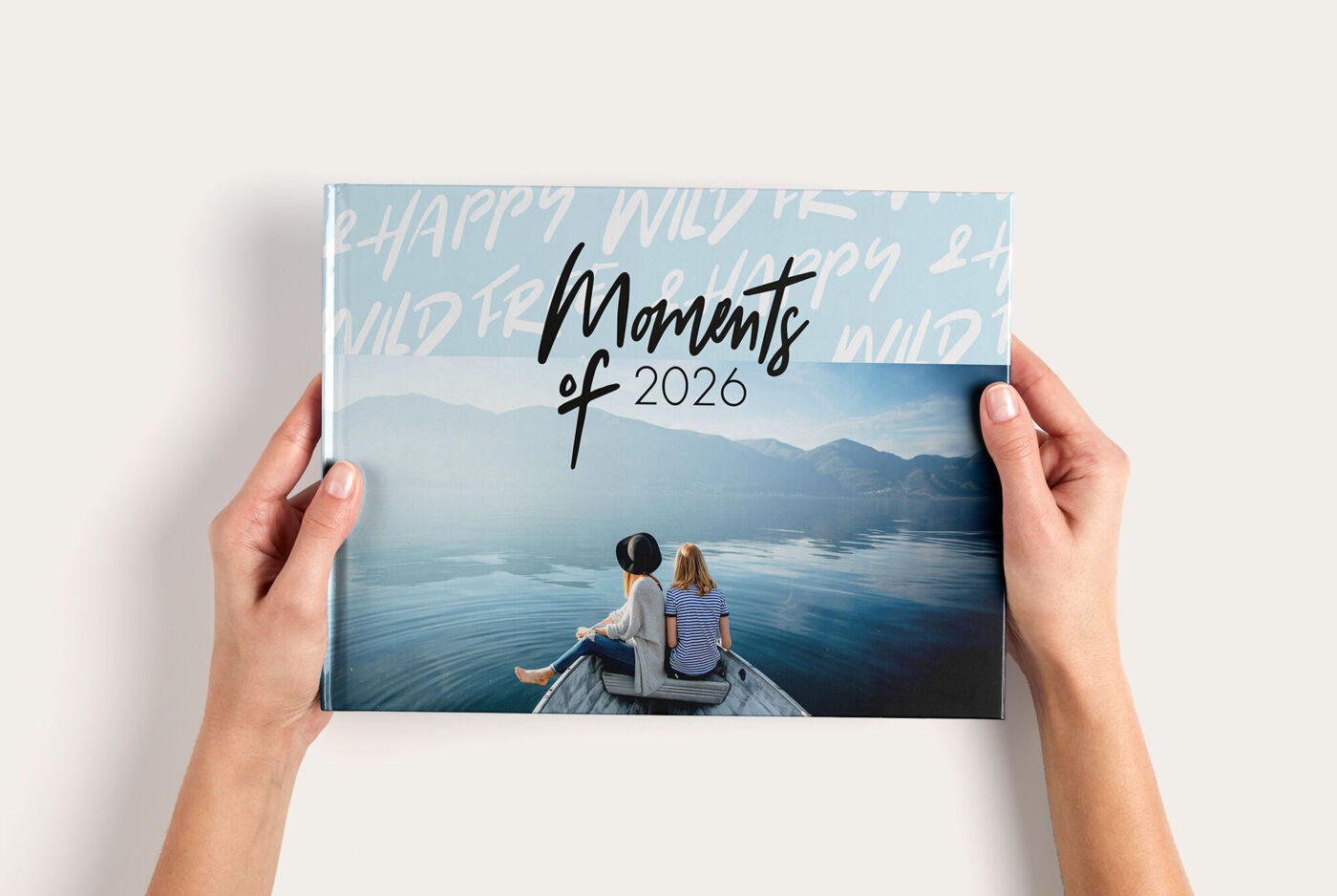 Zwei Personen sitzen auf einem Steg und halten ein CEWE FOTOBUCH mit dem Titel 'Moments of 2024'.