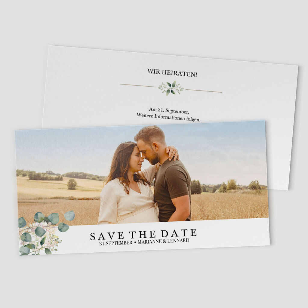 Ein Paar in einer schönen Landschaft, das Save-the-Date-Karten für ihre Hochzeit präsentiert.