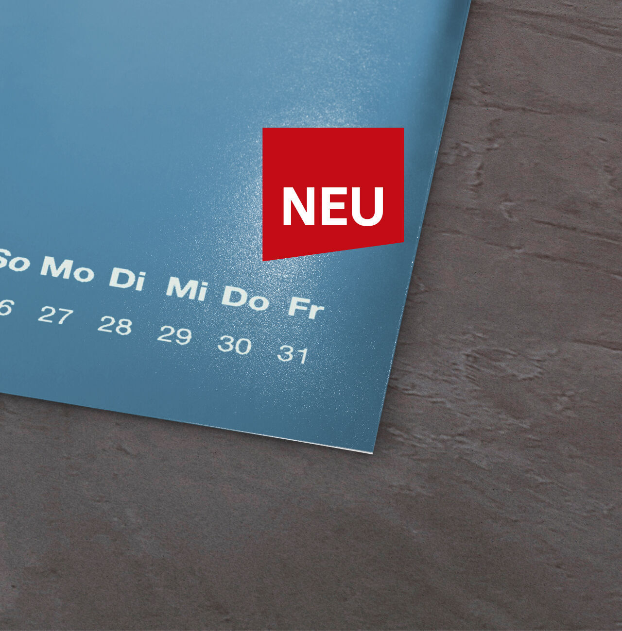 Kalenderblatt mit Wochentagen und dem Hinweis 'NEU' in rotem Feld