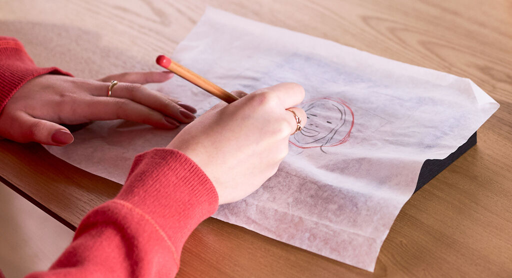 Eine Frau zeichnet einen Kreis auf Pergamentpapier, das auf einem eingerahmten Foto liegt.