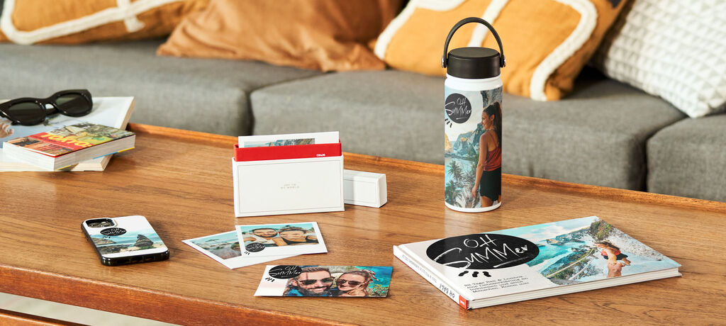 Eine inspirierende Zusammenstellung personalisierter Geschenke auf einem Holztisch, darunter ein CEWE FOTOBUCH, Fotos, eine Trinkflasche und ein Smartphone.