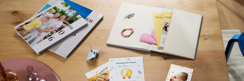 Ein CEWE Fotobuch liegt offen auf einem Holztisch mit verschiedenen persönlichen Erinnerungen, wie Grußkarten und einem bunten Armband.