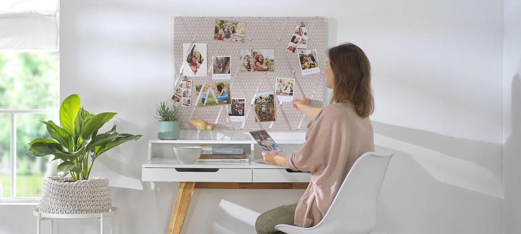 Eine Person gestaltet eine Fotocollage an einer Wand mit Bildern und Pflanzen auf dem Tisch, um Erinnerungen zu teilen