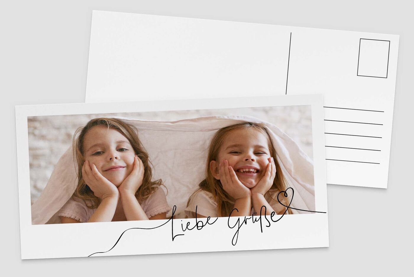 Zwei Mädchen sitzen unter einer Decke und halten sich die Hände vor das Gesicht. Auf der Karte steht 'Liebe Grüße'.