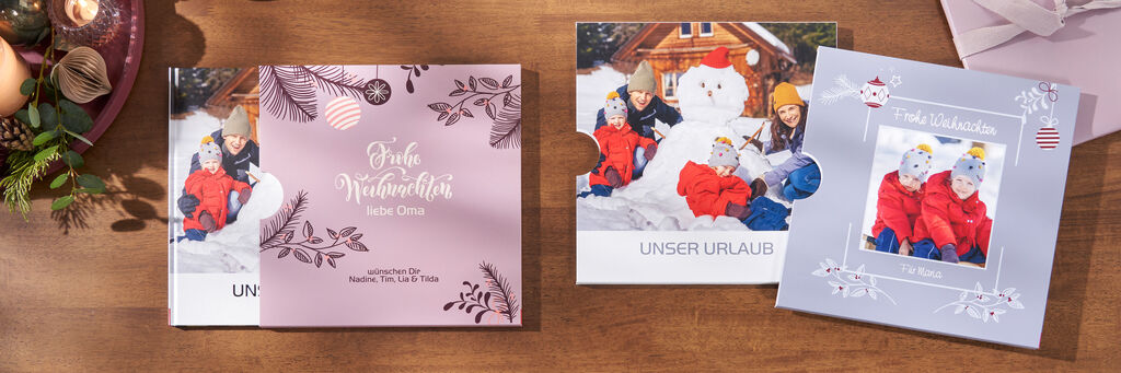 Zwei CEWE Fotobücher liegen auf einem Tisch. Eines zeigt Kinder in Winterkleidung vor einem Schneemann, das andere hat eine weihnachtliche Gestaltung.