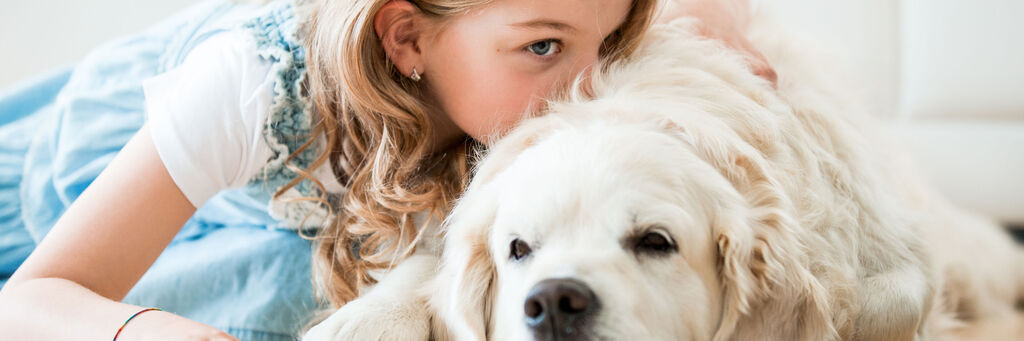 Ein glückliches Kind mit einem Golden Retriever, das auf dem Boden spielt und kuschelt