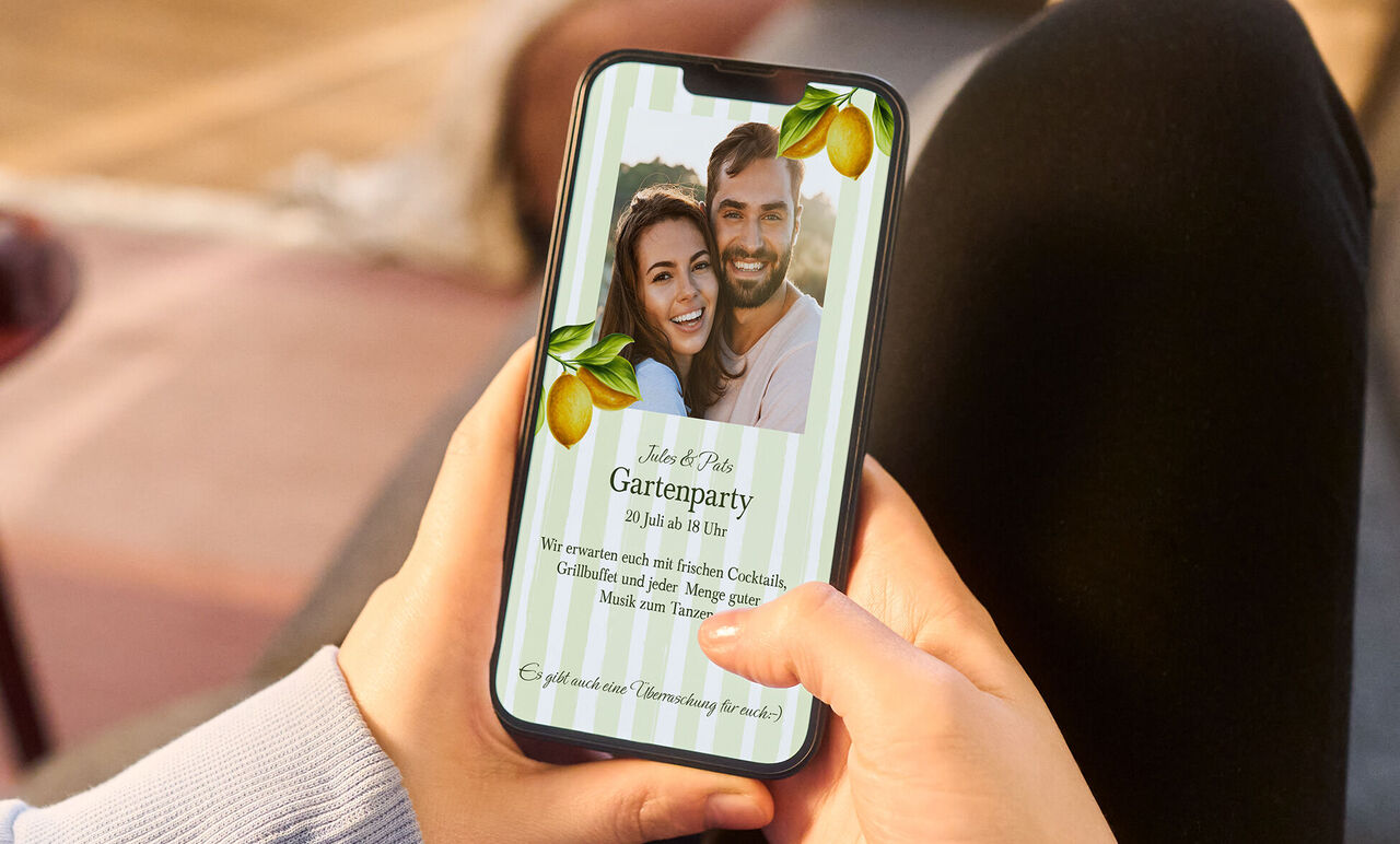 Ein Smartphone wird in den Händen gehalten, auf dem Bildschirm ist die digitale Einladungskarte in einem sommerlichen Design zu sehen.