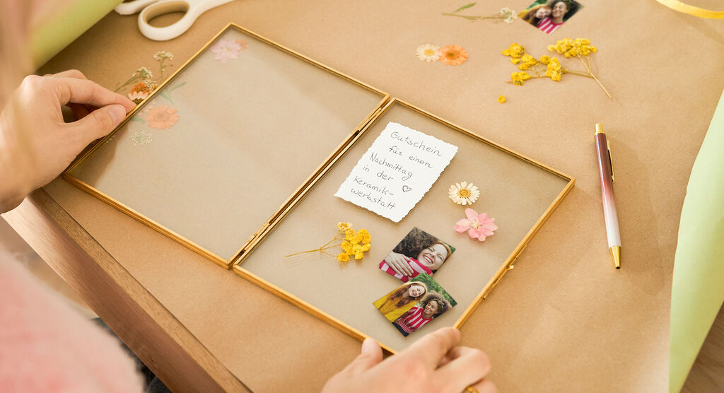 Zwei Hände gestalten eine liebevolle Erinnerungsbox mit Blumen und Fotos