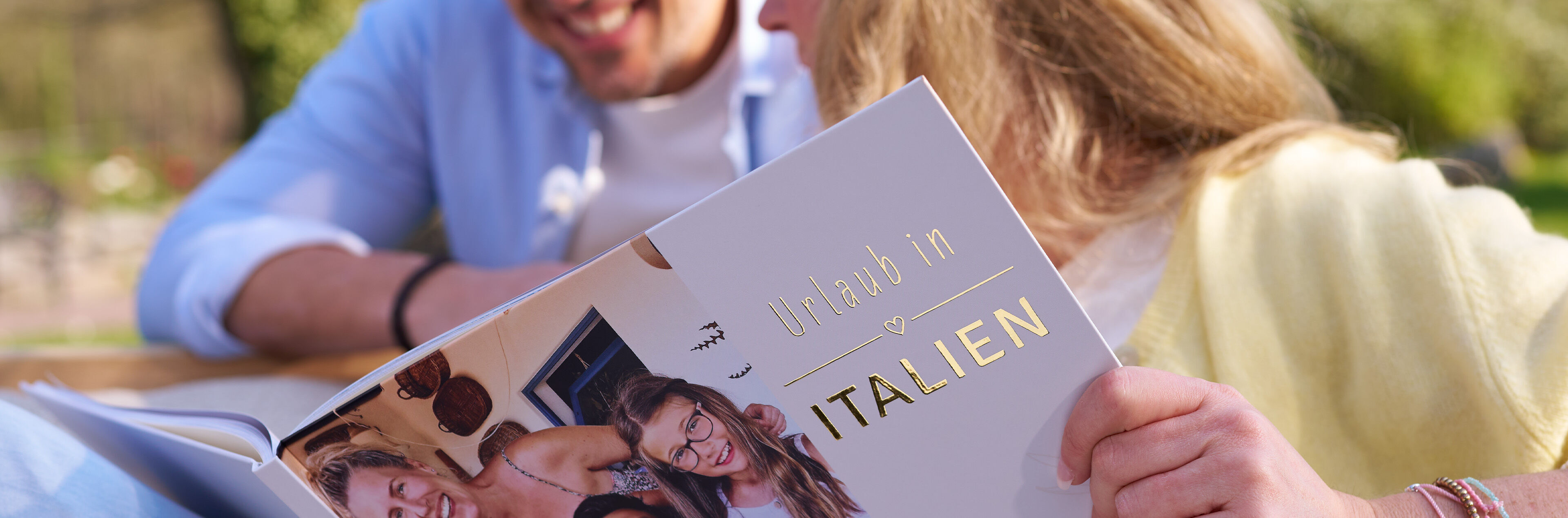 Person hält ein Fotobuch mit der goldenen Aufschrift „Urlaub in Italien“.