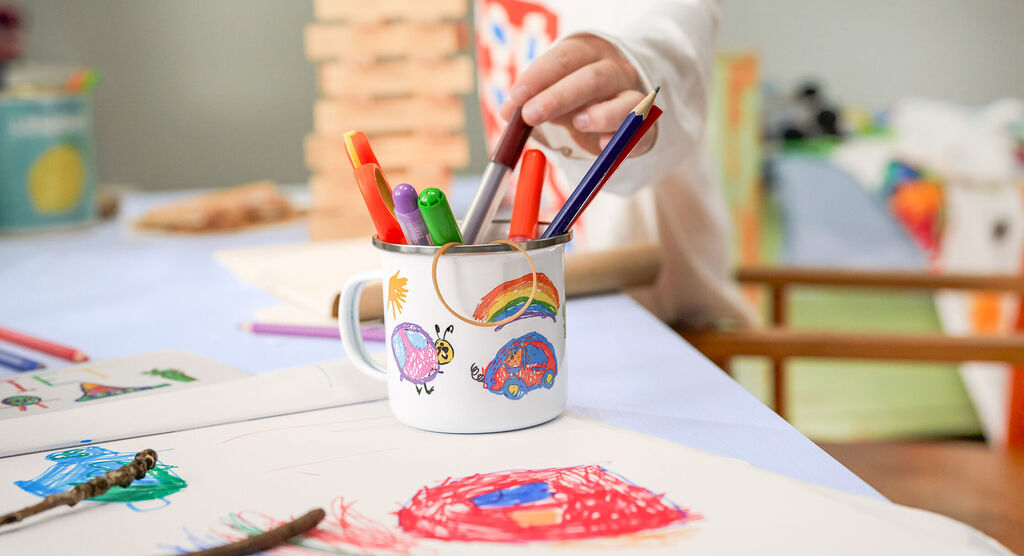 Bunte Stifte in einem Becher, Hand eines Kindes greift nach einem