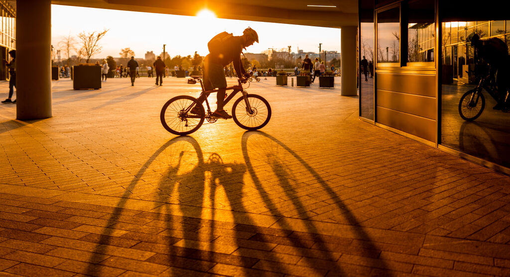 Ein Radfahrer fährt bei Sonnenuntergang durch ein modernes Stadtambiente und wirft längliche Schatten.
