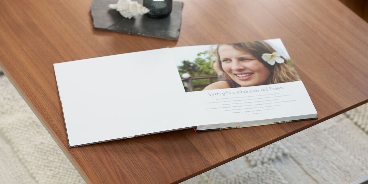 Ein geöffnetes Fotobuch auf einem Holztisch mit einer weißen Seite und einer Bildseite mit floralen Elementen