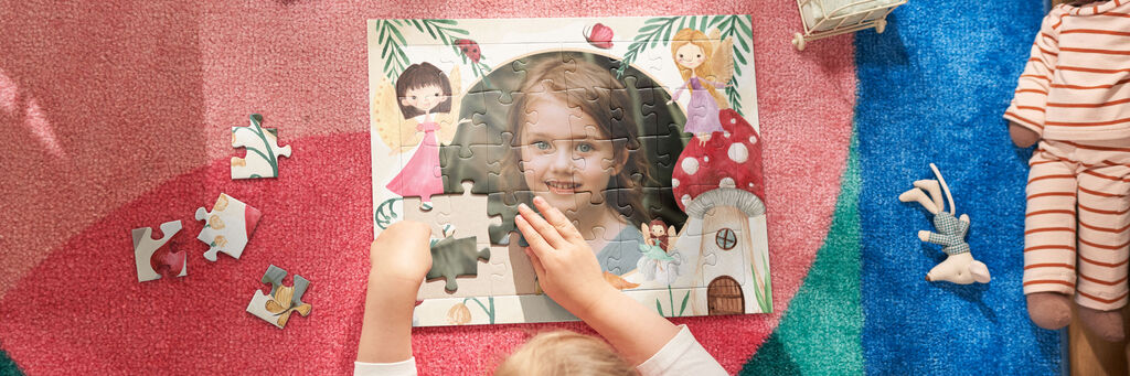 Ein Kind setzt Puzzlestücke in ein farbenfrohes Puzzle ein. Das Puzzle zeigt eine fröhliche Szenerie mit Tieren und Menschen.