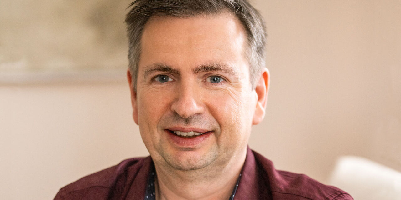 Ein lächelnder Mensch in einem gemütlichen Raum, der Freude ausstrahlt. Der Hintergrund ist weich und beruhigend.