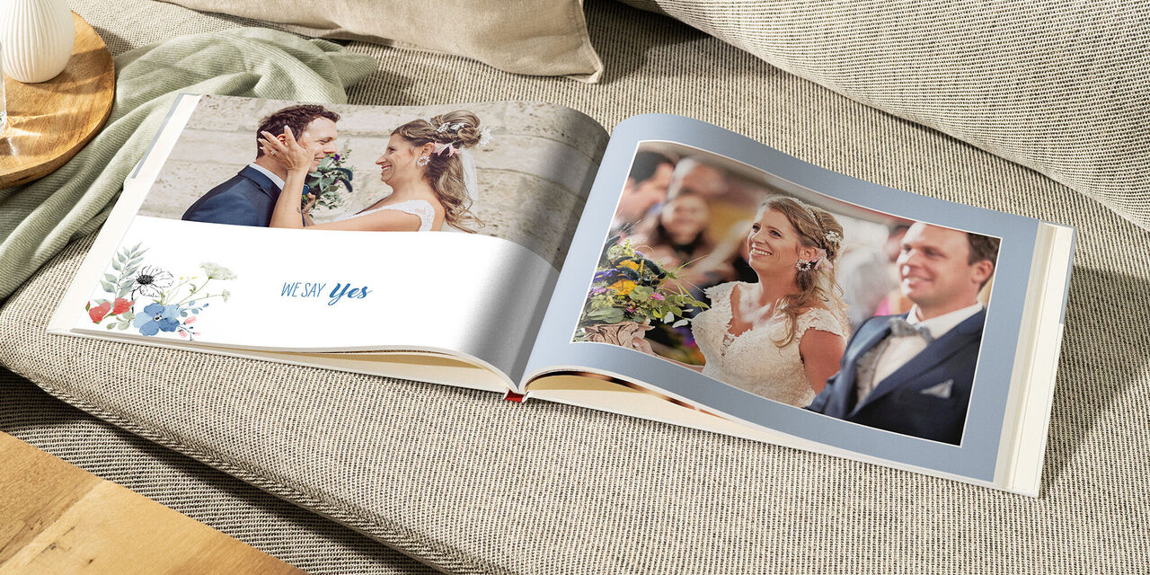 Ein geöffnetes Fotobuch auf einem gemütlichen Sofa zeigt eine romantische Hochzeit. Es sind schöne Erinnerungen abgebildet, die die Freude des Paares widerspiegeln.