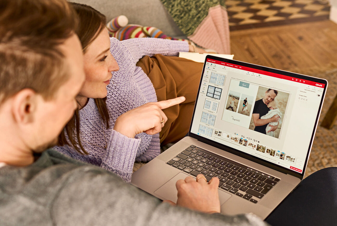 Paar gestaltet ein CEWE Fotobuch am Laptop mit eigenen Bildern