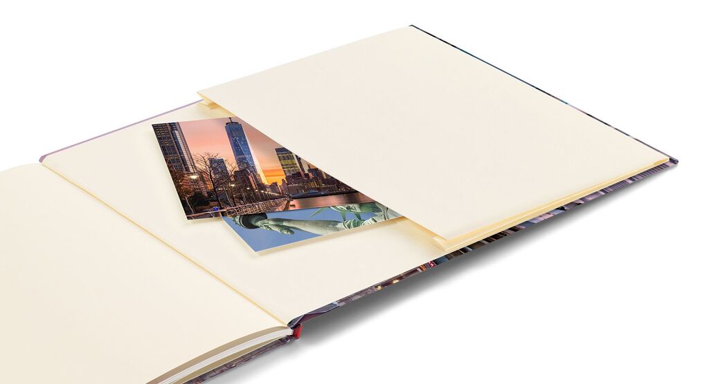 Ein offenes CEWE FOTOBUCH zeigt leere Seiten und zwei Fotos, die in eine Hülle gesteckt sind.