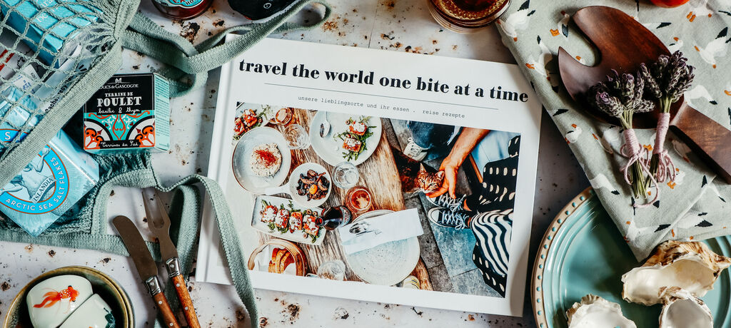 CEWE FOTOBUCH mit Fotos von Speisen; Titel "travel the world one bite a time". Umgeben von maritimen Accessoires.