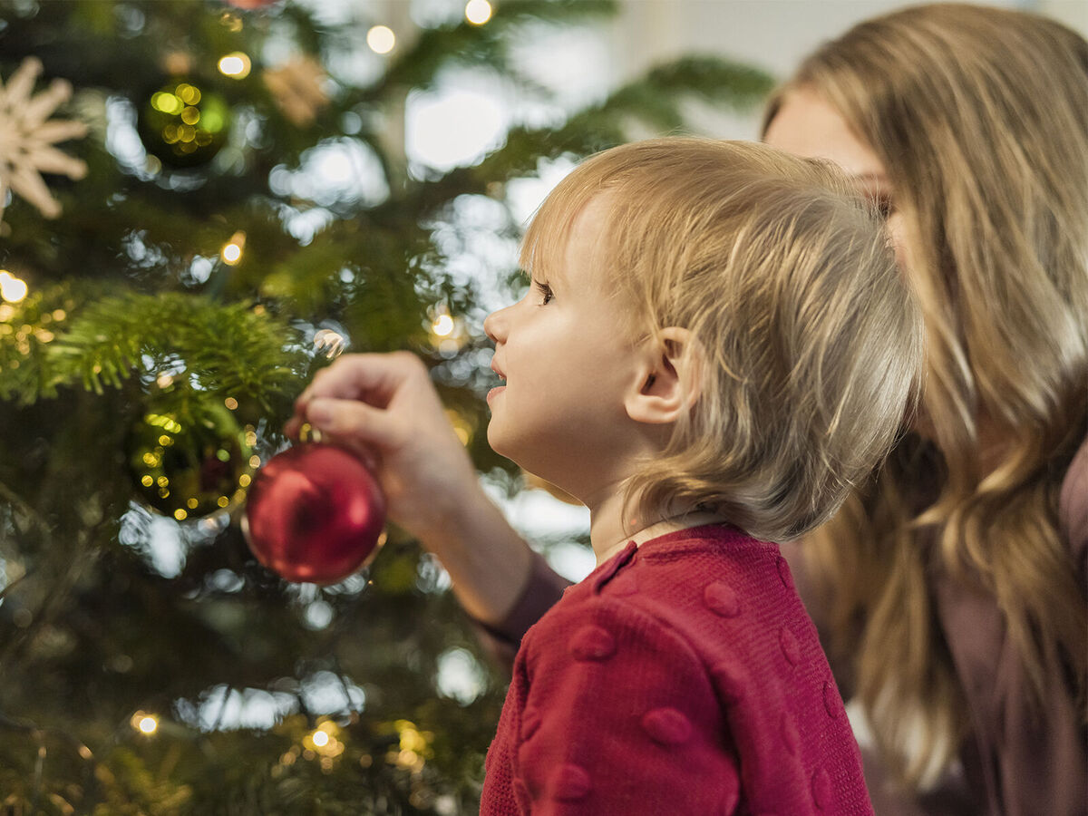 Ein Kind und eine Erwachsene dekorieren einen Weihnachtsbaum mit bunten Kugeln.