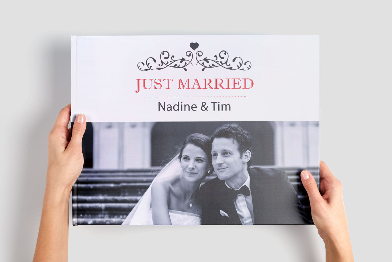 Hände halten ein CEWE FOTOBUCH mit dem Titel 'Just Married' und den Namen 'Nadine & Tim'